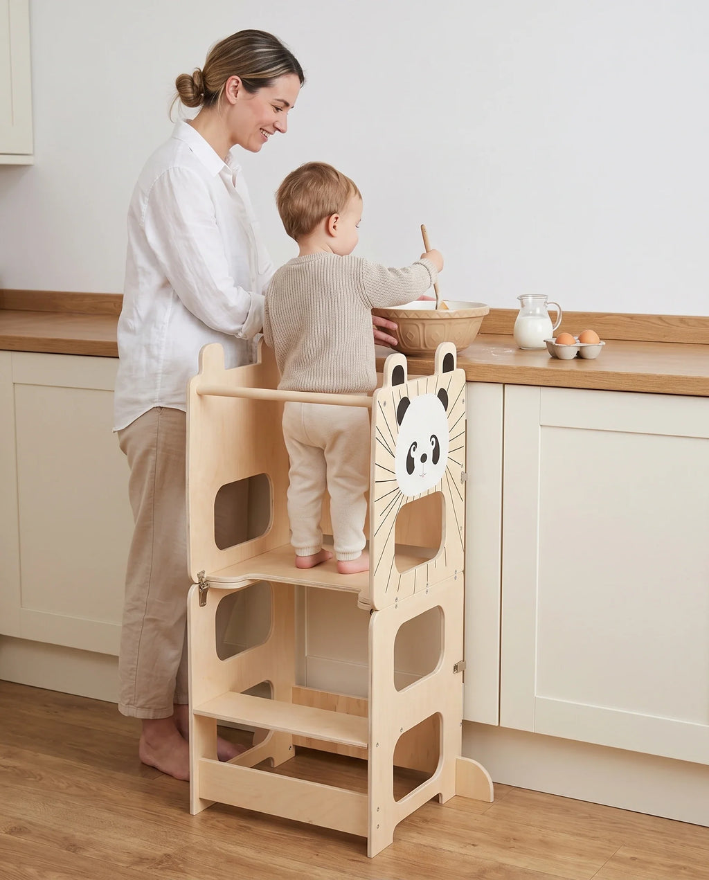 Enfant sur sa tour d'observation, à hauteur du plan de travail, qui cuisine avec sa maman